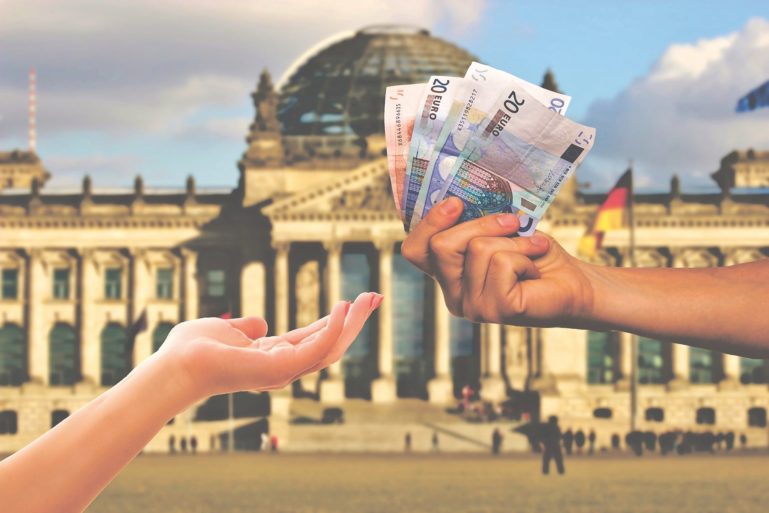 Hand gibt anderer Hand Geld vor dem Reichstagsgebäude